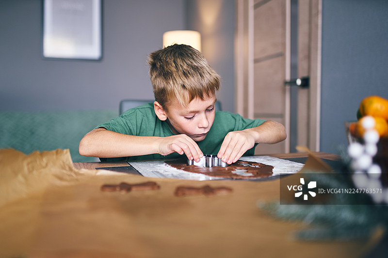 小男孩在家烘焙过节食品时，专注地切割巧克力形状图片素材