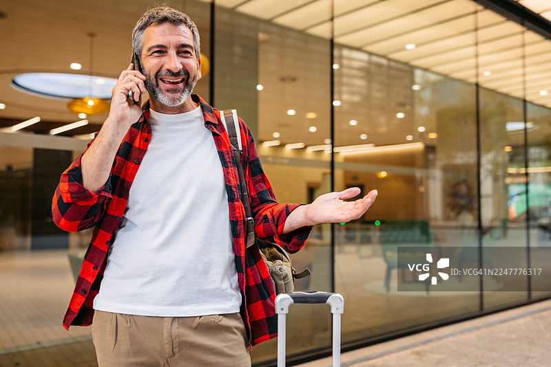 一位成熟的男士在西班牙巴塞罗那街头，带着带轮子的行李箱，正在打电话。图片素材
