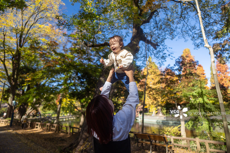 母亲在公园里抱着女婴高举向天空图片素材