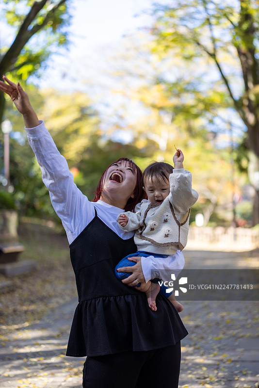 妈妈抱着女婴，抬头望着公园里的秋叶图片素材