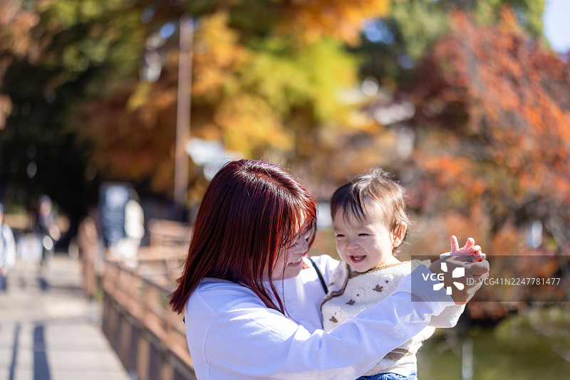 母亲抱着她的女婴站在公园的步行桥上图片素材