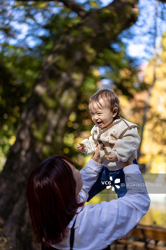 一位母亲在公园里举着婴儿，欣赏着秋叶图片素材