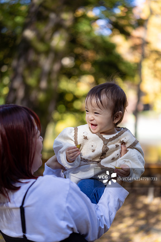 一位母亲抱着婴儿女孩，在公园里欣赏秋叶图片素材