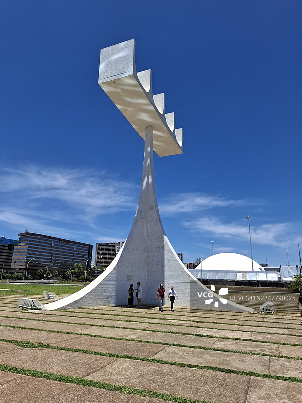 巴西利亚都会大教堂的标志性钟楼下，一群游客正在荫凉处避暑。图片素材