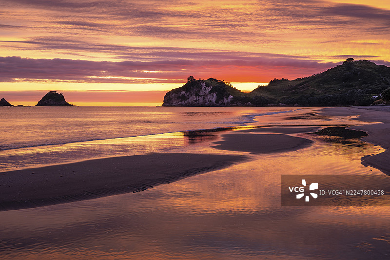 新西兰海景和沙滩风光。日出时分的哈海伊海滩及特帕雷角。左侧为特卡拉克岛岩石。彩色云朵。哈海伊,科罗曼德半岛,怀卡托,新西兰图片素材