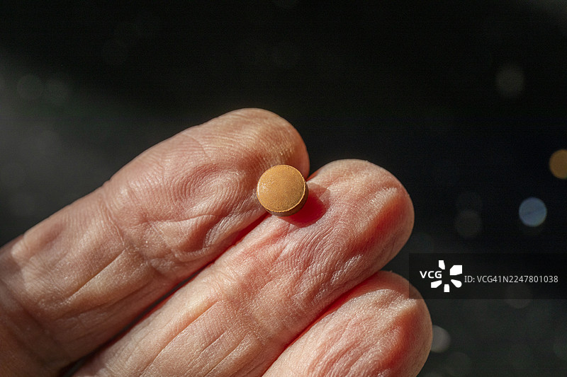 服用铁补充剂——一颗富马酸亚铁药片放在一位老年男子的手指上图片素材