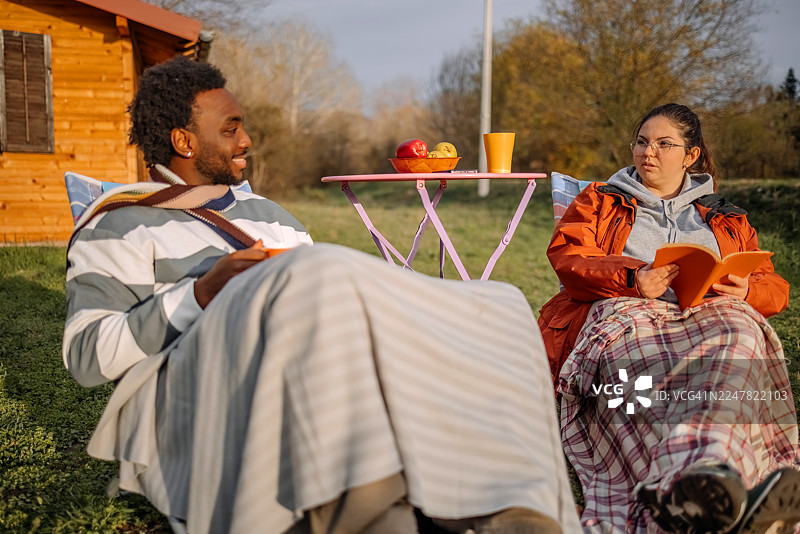 秋日暖阳下，人们在小屋前悠闲地坐着读书图片素材