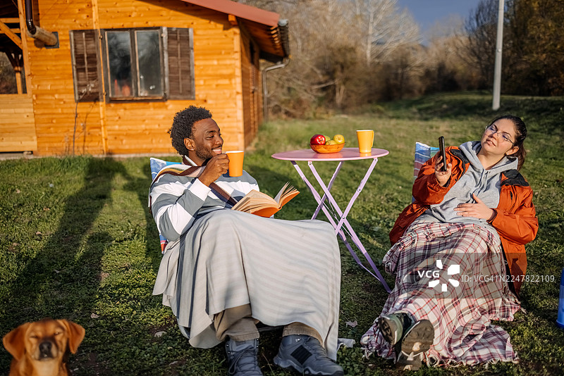秋日暖阳下，人们悠闲地坐在小屋前，各自玩着手机。图片素材