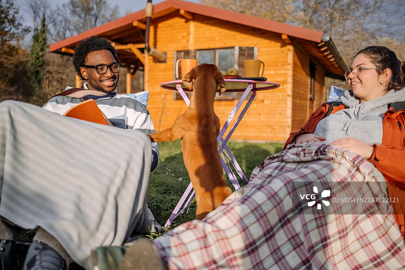 秋日暖阳下，人们在郊区别墅前放松，与宠物玩耍，并阅读书籍。图片素材