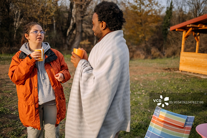 秋日暖阳下，人们站在小屋前放松地交谈。图片素材