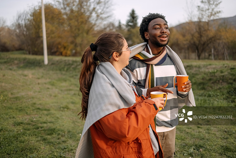 秋日暖阳下，人们在小屋前站着交谈，悠闲放松。图片素材