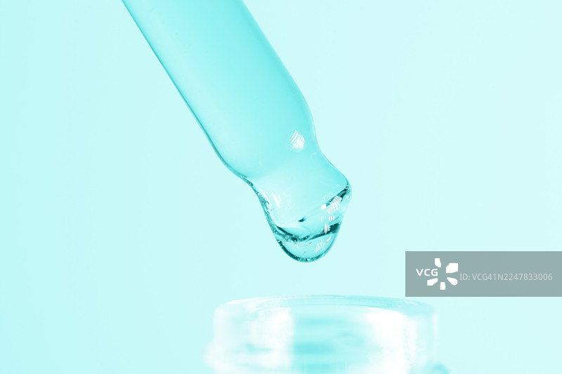 蓝色背景下，滴管正滴下液体至瓶中，特写镜头展示液体转移，适用于科学、健康或美容品牌，概念涉及药物、精华液或化学试剂滴，是药店、化妆品系列或实验室的理想选择图片素材