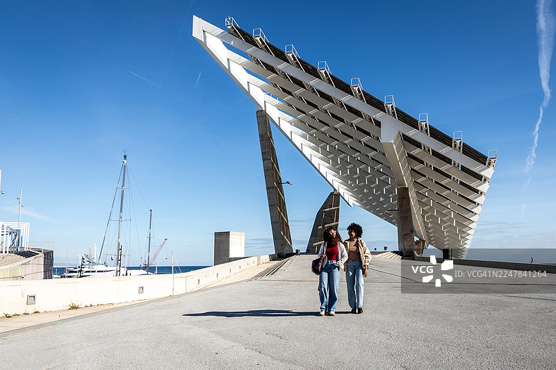 两位成年女性在大型太阳能电池板结构附近行走图片素材