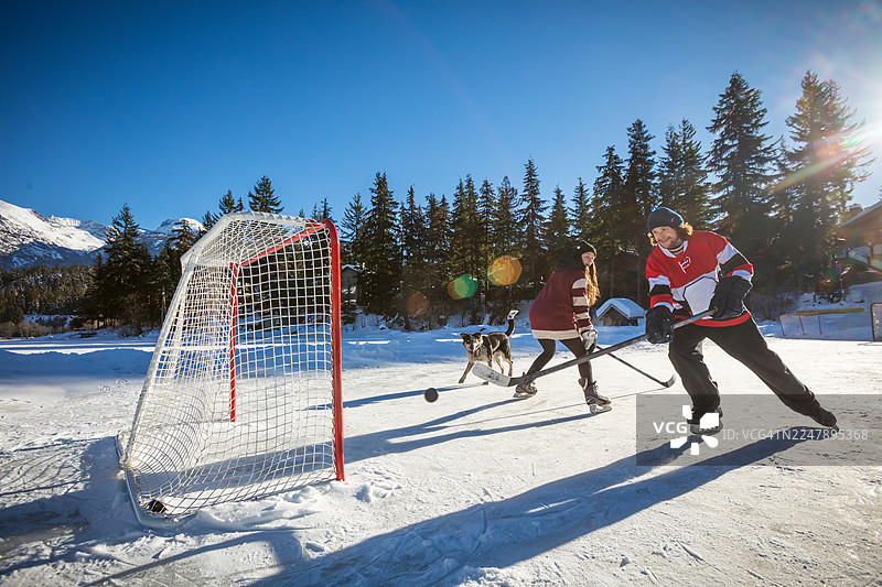 年轻男子与狗在惠斯勒的池塘上打冰球图片素材