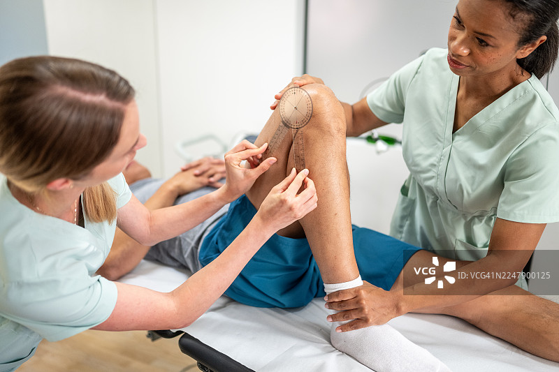 临床环境下，医护人员对患者膝盖进行评估的中景镜头图片素材