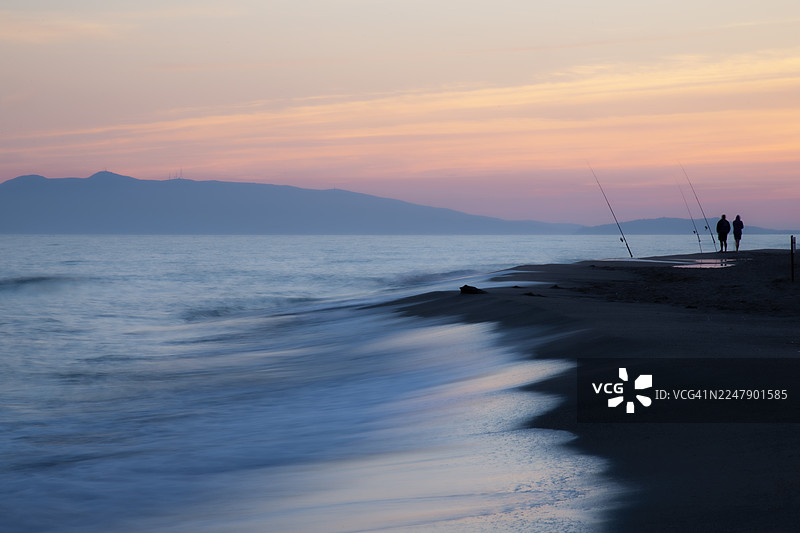 长曝光和柔焦效果，拍摄了在蓝色时刻的海滩上剪影状的两位渔民图片素材