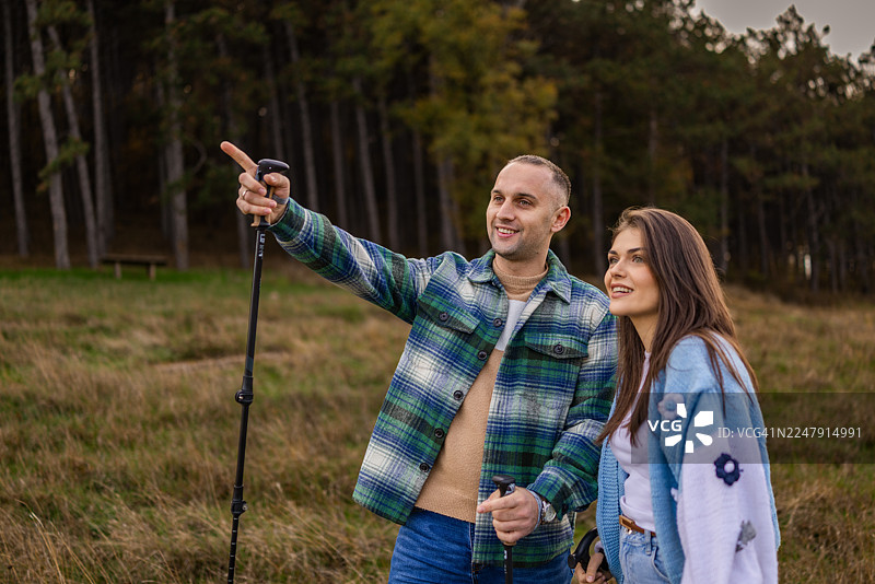 一位英俊的男子在森林里徒步旅行时，手指着远方，他的朋友也在旁边。图片素材