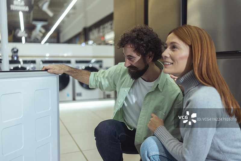 一对热恋中的无忧情侣在电子产品商店里，兴致勃勃地探索展示的冰箱功能。图片素材