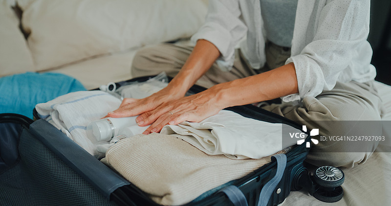 特写：年轻亚洲女性在家卧室的床上准备衣物和个人物品，打包行李箱，为轻松的夏季度假旅行做准备。图片素材