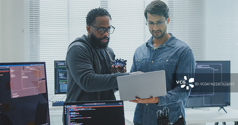 黑人和西班牙裔男性工程师程序员在科技办公室合作开发机器人手原型，使用计算机控制的机械臂电路。软件开发，人工智能。图片素材