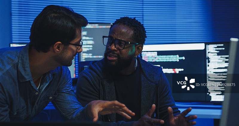 黑人和西班牙裔男性工程师程序员在科技办公室通宵合作，讨论软件开发策略。软件开发人员，人工智能。图片素材