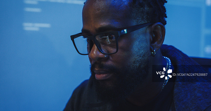 特写：一名黑人工程师程序员在科技办公室对着电脑工作，制定软件开发策略，直至深夜。软件开发者，人工智能概念。图片素材