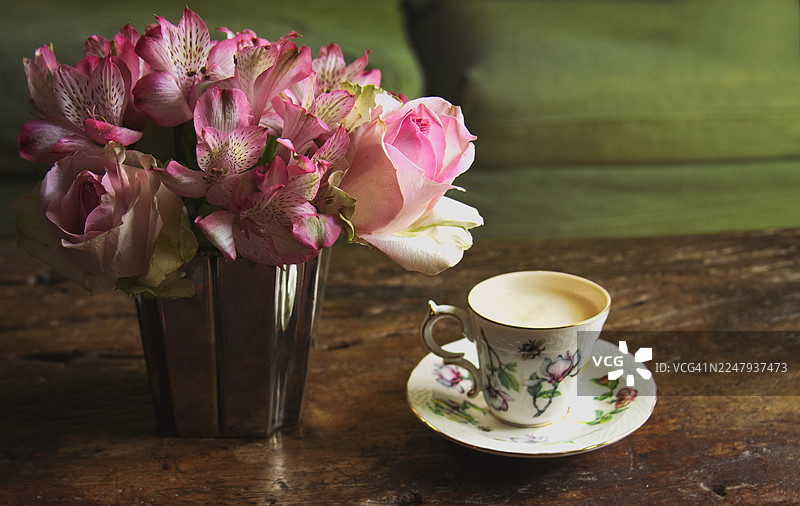 粉色玫瑰和陶瓷咖啡杯放在木质咖啡桌上。静物。图片素材