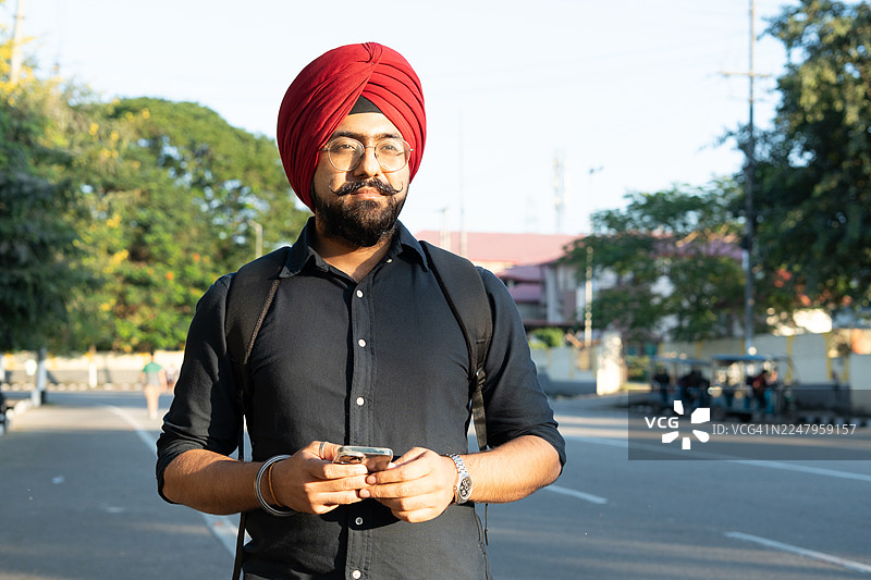 年轻的印度男子在户外使用手机。图片素材