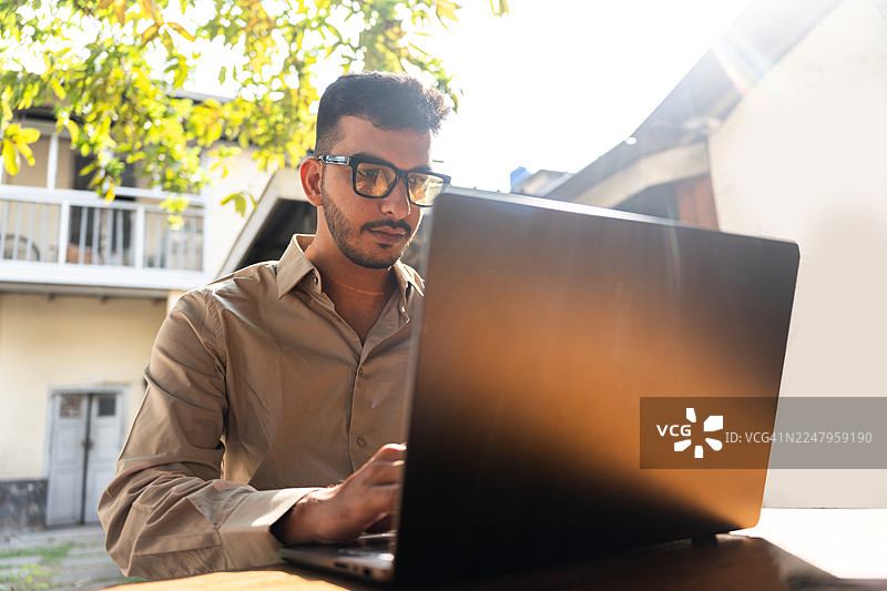 一位年轻的印度男子在户外咖啡馆使用笔记本电脑。图片素材