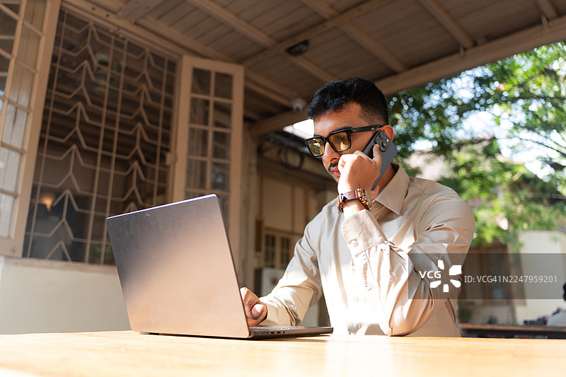 一位年轻的印度男子在户外咖啡馆使用笔记本电脑。图片素材