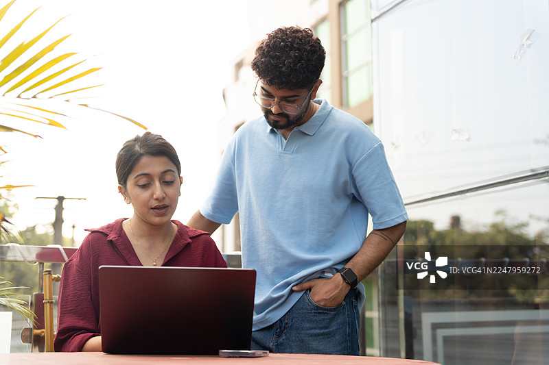 两个年轻人正在庭院里讨论并使用笔记本电脑工作。图片素材