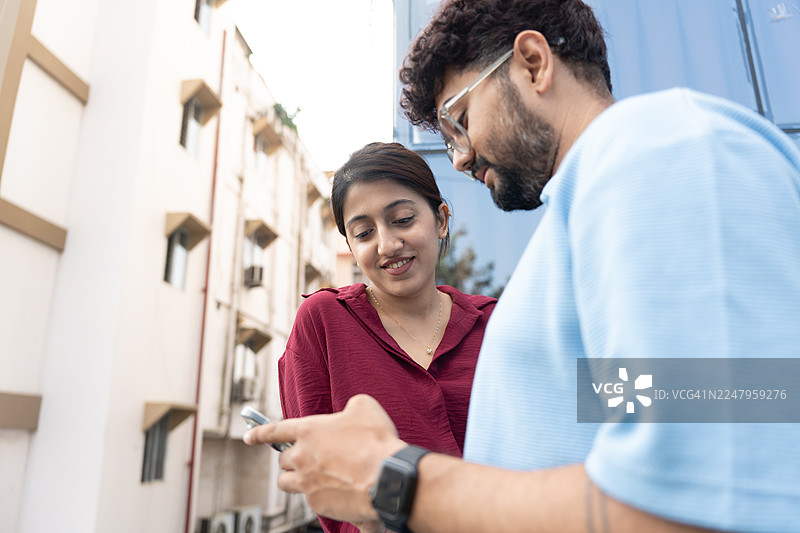 两个年轻人一边讨论一边在手机上查看内容。图片素材