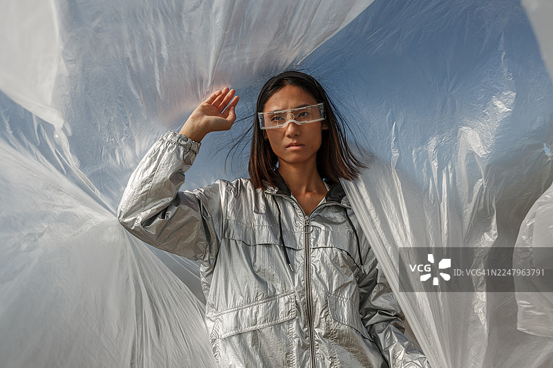 一位年轻的亚洲女性，身着银色套装，佩戴未来感眼镜，站在阿尔梅里亚的半透明塑料薄膜下。图片素材