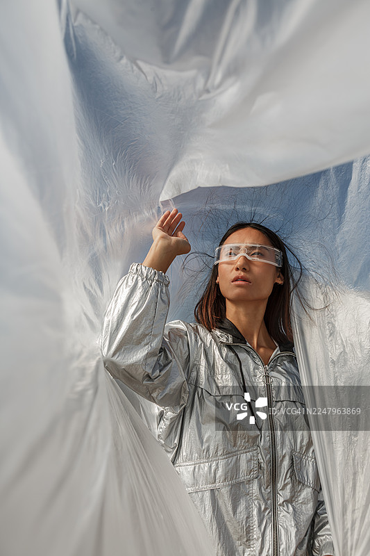 身穿银色套装、戴着未来感眼镜的年轻亚洲女性在户外半透明塑料中摆姿势图片素材