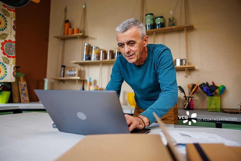 老年男子在厨房用笔记本电脑阅读财务数据图片素材