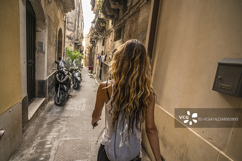 一名女游客走在西西里锡拉库萨奥提伽老城一条狭窄的街道上图片素材