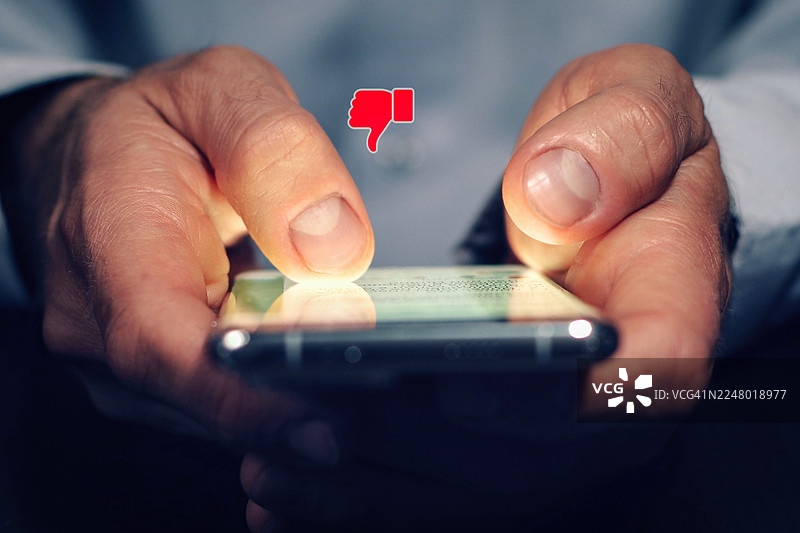 夜间，一名男子在智能手机上对社交媒体内容表示不满。他正在给出负面反馈、网上评价并表达不赞同。图片素材