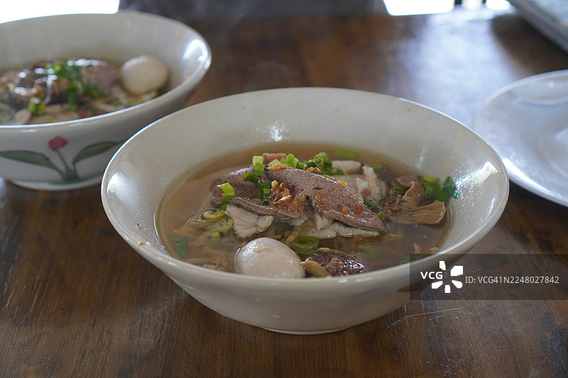 泰式面条，白色碗中盛有小面条、炖猪肉、肉丸、猪肝和血汤，配以木筷和勺子，用调味料调味，泰式美味佳肴图片素材
