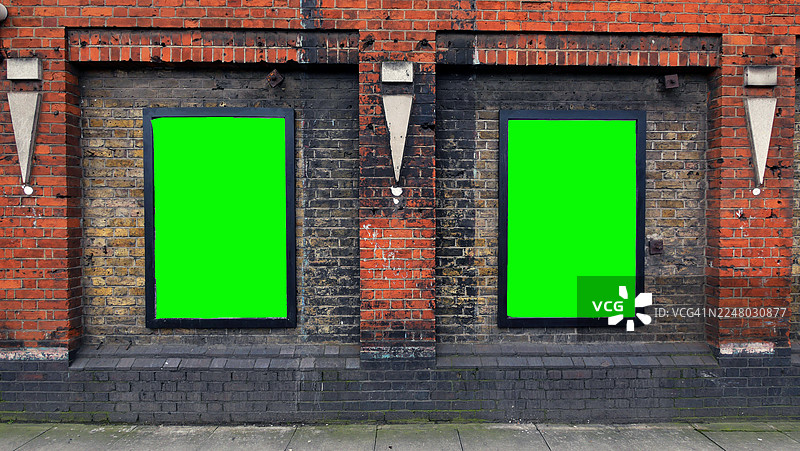 老旧风化的砖墙上，有两个绿色背景的标志。英国伦敦。铺砌的人行道。阳光。自然色彩。图片素材