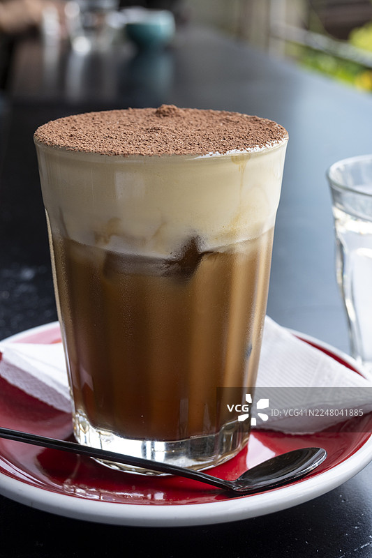 近距离展示一杯冷藏的越南鸡蛋咖啡，上面撒有可可粉，突显其奶油般的层次和独特的风格。图片素材