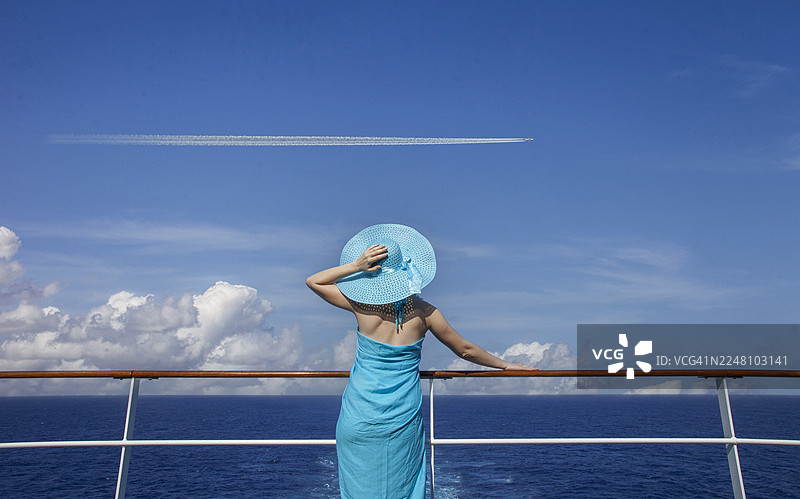 一名女子在游轮上观看天空中飞行的飞机。图片素材