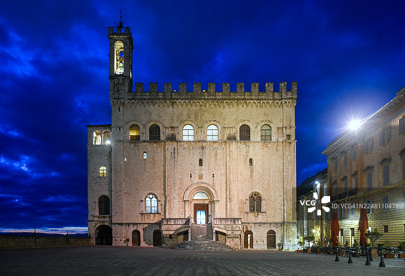 意大利翁布里亚古比奥市，古比奥市政厅（又名“领主宫”）雄伟的立面在黄昏之夜被点亮，背景是古比奥大广场上戏剧性的天空。图片素材