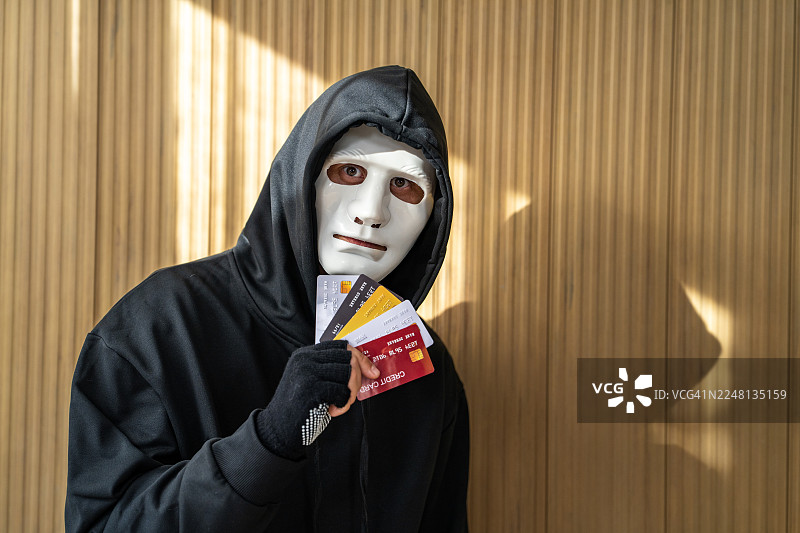 戴着面具的黑客，手中持有偷来的信用卡图片素材