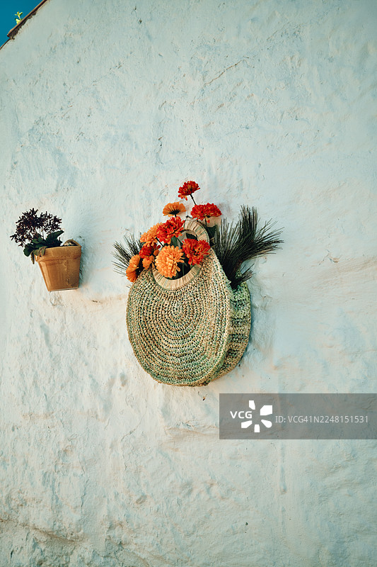 挂在粉刷墙上的草编包，旁边有鲜花图片素材