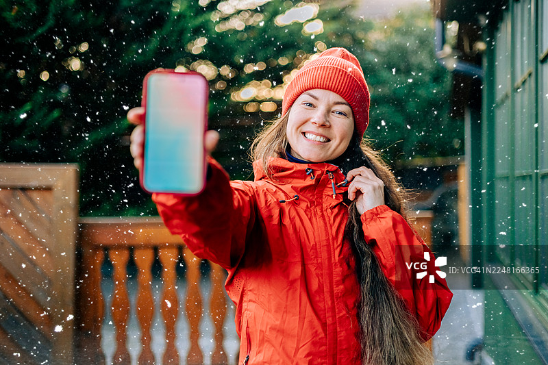 一位女性在冬季节日季展示带有手机模型界面的智能手机屏幕图片素材