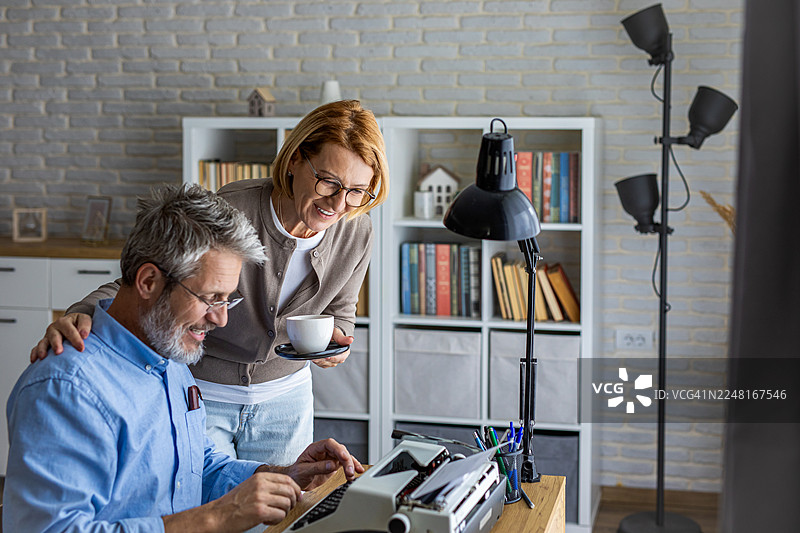 微笑的女人看着一个男人在老式打字机上打字图片素材