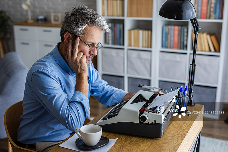 一位男士在老式打字机上打字时思考图片素材