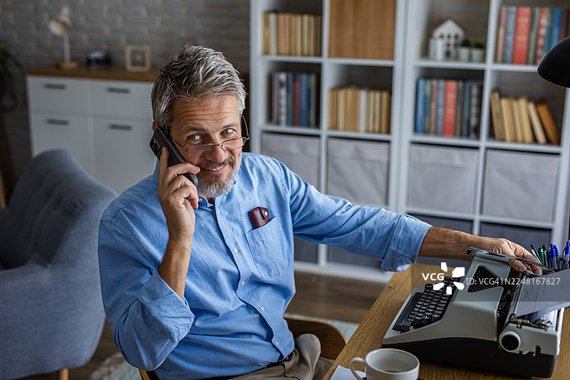 居家办公空间里，一位男士正在用智能手机通话图片素材
