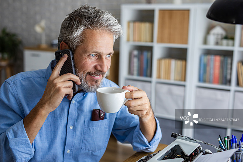 居家办公的男人一边喝咖啡一边用智能手机打电话图片素材