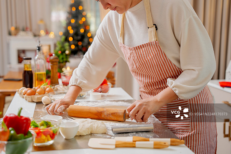 亚洲女性在家中的厨房为圣诞派对制作自制披萨，迎接假期。图片素材